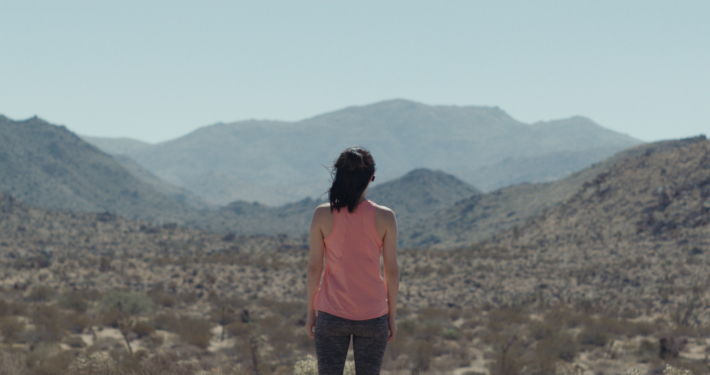 A woman stands alone facing distant mountains in the Mojave Desert in 29 Palms.