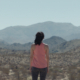 A woman stands alone facing distant mountains in the Mojave Desert in 29 Palms.
