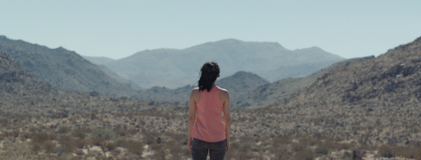 A woman stands alone facing distant mountains in the Mojave Desert in 29 Palms.